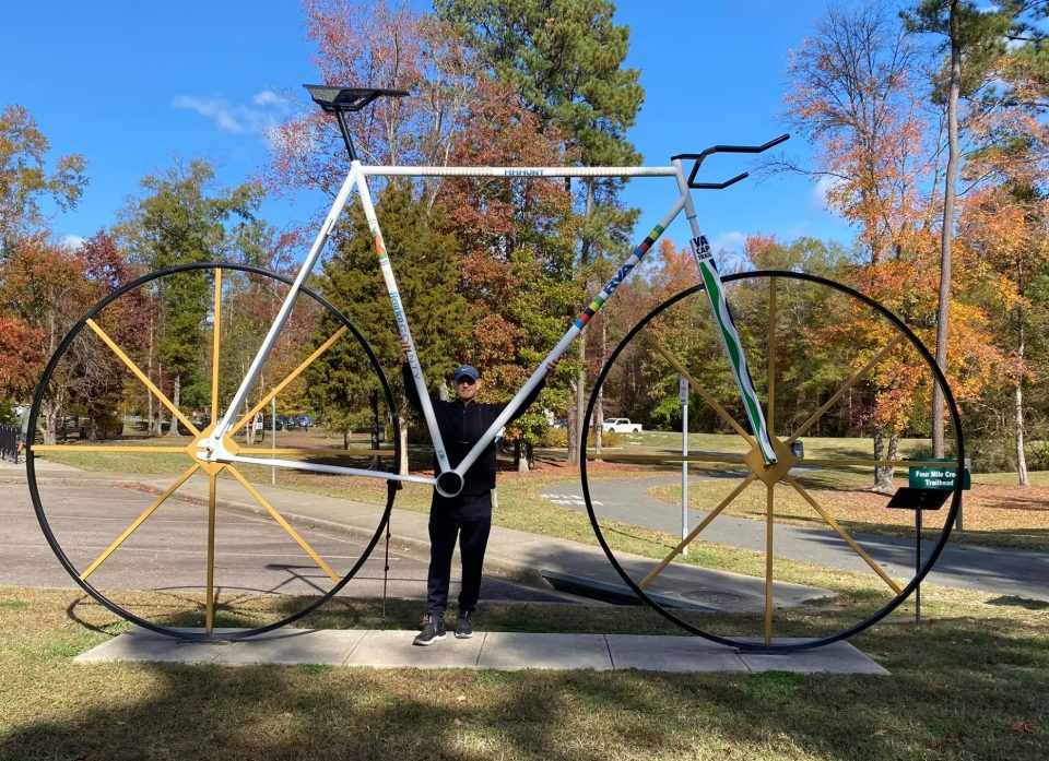 A participant standing inside the giant bicycle sculpture at the Four Mile Creek Trailhead