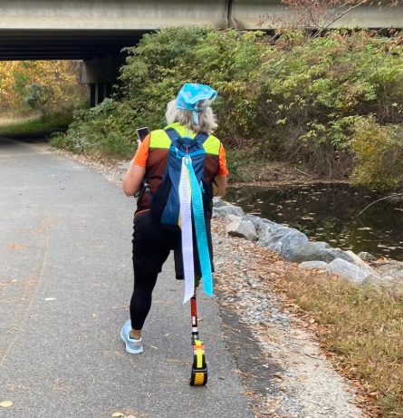 A walker with ribbons on her pack passing under a bridge on the trail